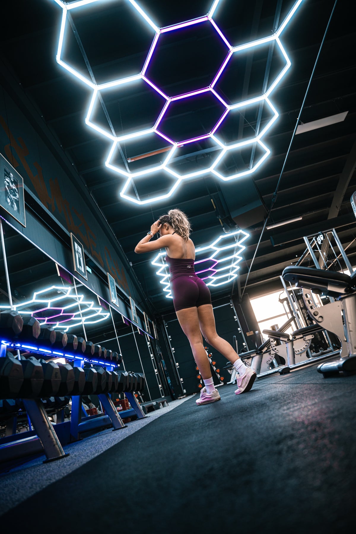 Atlete in de Extreme-set in Dark Coffee bij het dumbbellrek onder neonlicht